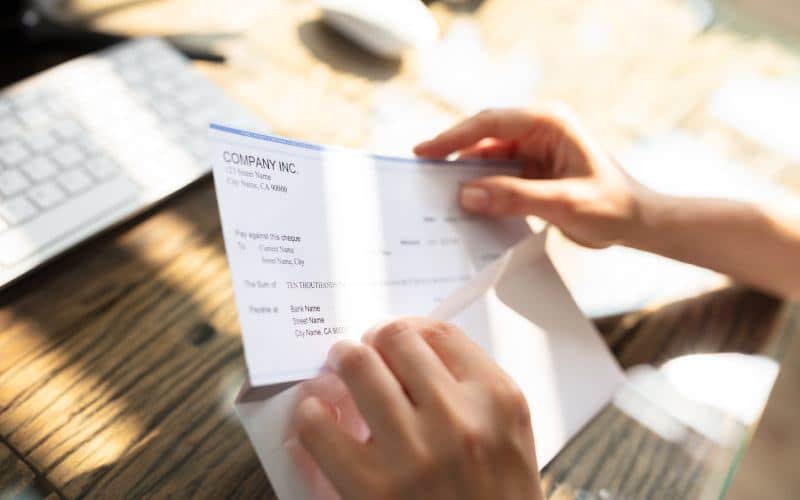 Close-up of an employee's hand opening envelope with paycheck over wooden desk
