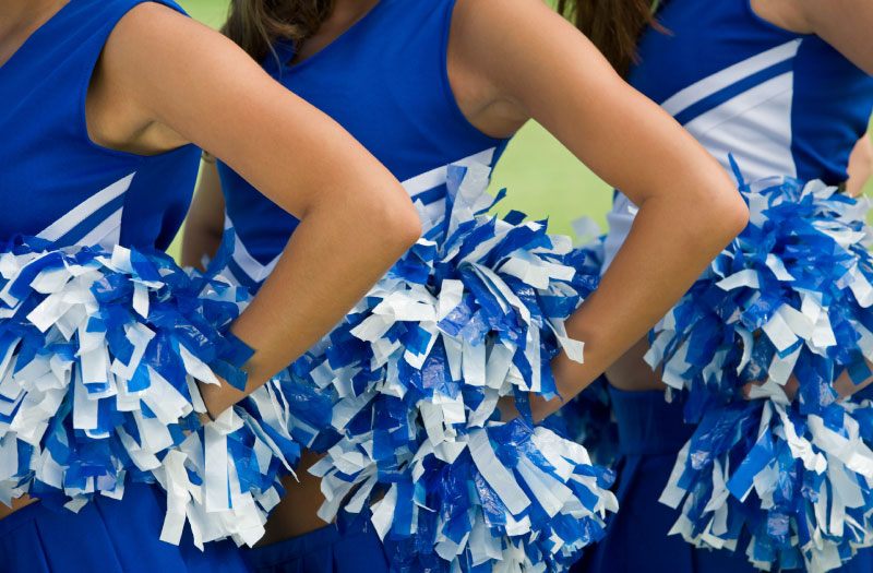 close-up of cheerleaders in blue and white uniforms with pom pons