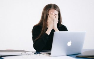 Woman With Hands on her Face in front of a Laptop