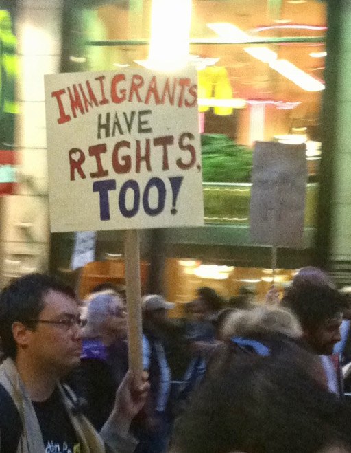 Several people marching, one carrying a sign that says "Immigrants have rights too!"