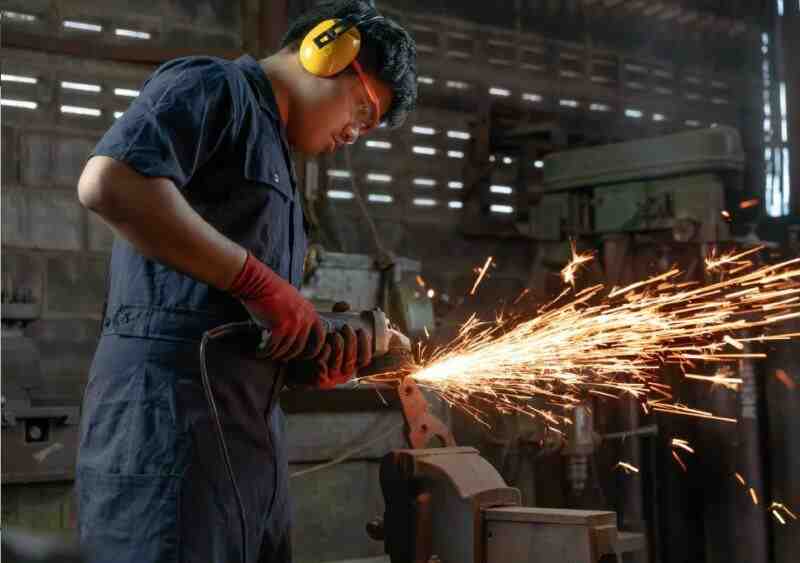 Asian Mechanical engineer operating power tools with metal sparks